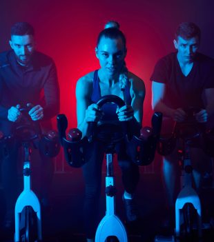 youth in the gym, exercising their legs doing cardio training, having spinning class at gym in dark neon lighted smoky space